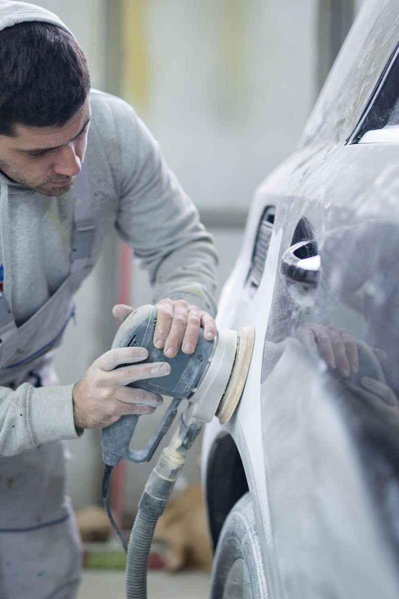 Panel beater sanding a car panel